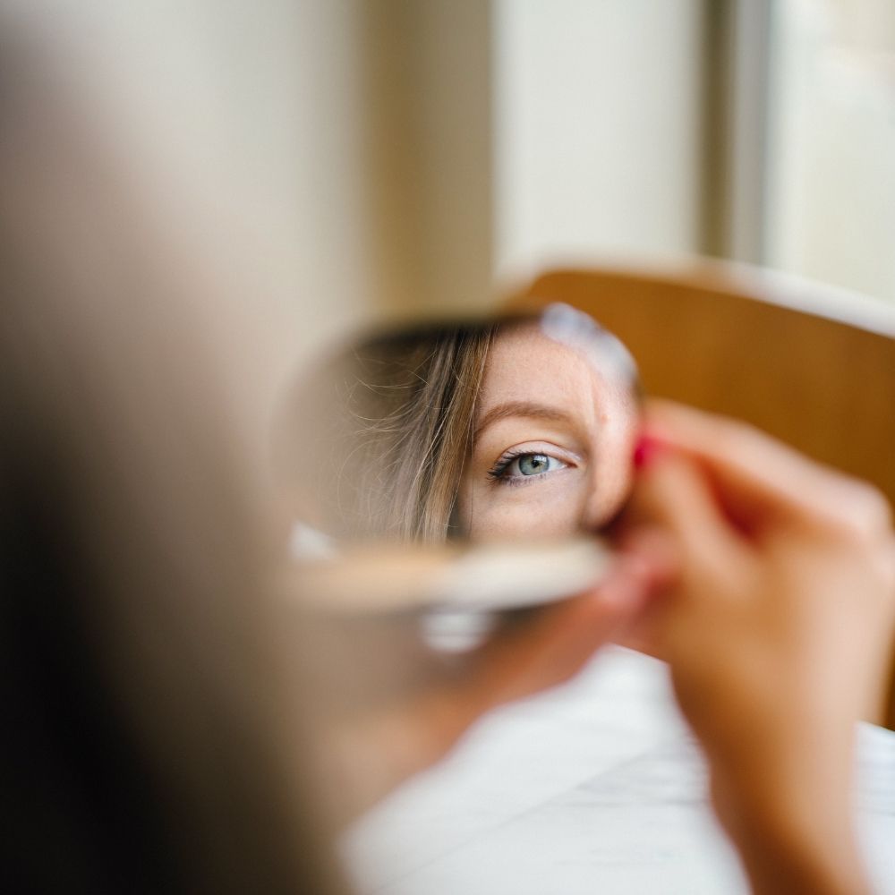 Mulher olhando para um espelho de mão