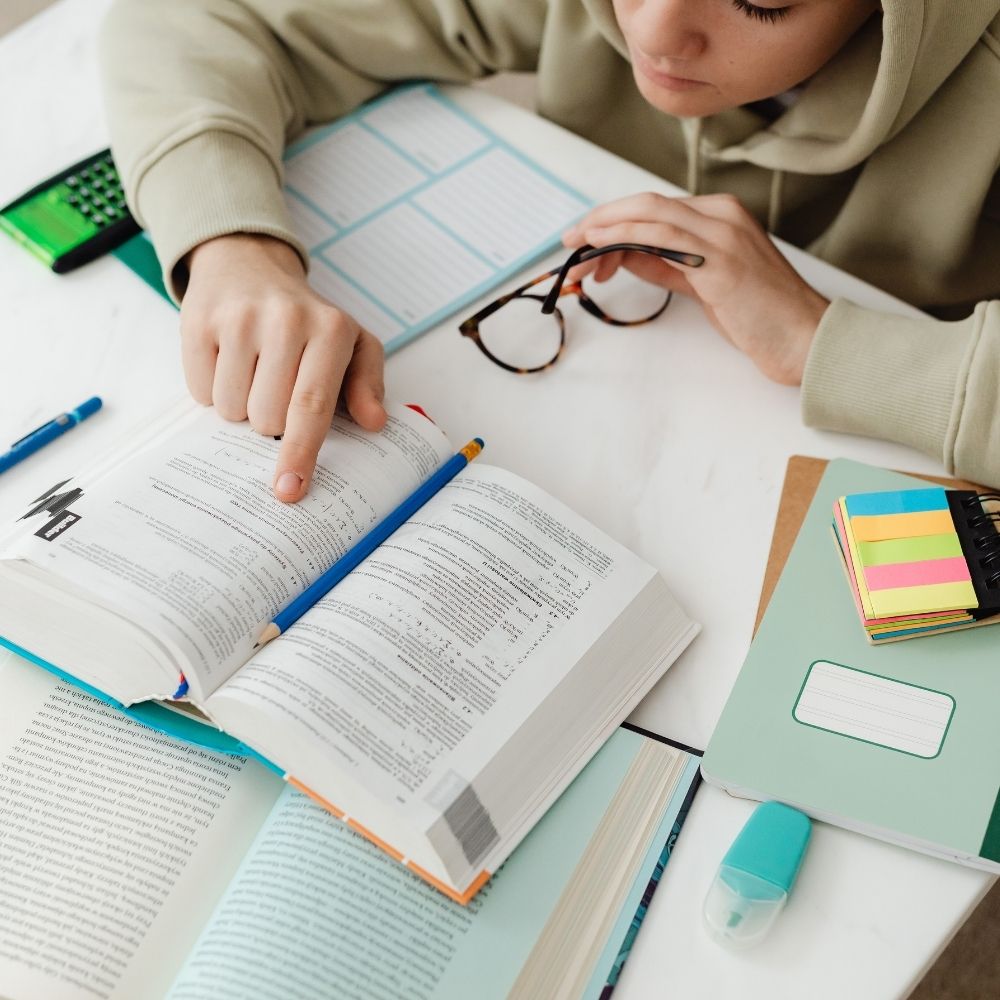 Adolescente estudando com livros e materiais escolares sobre a mesa